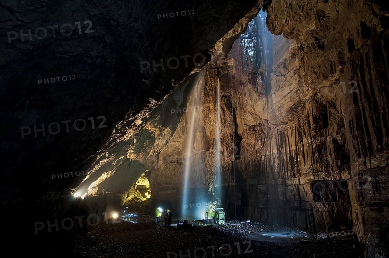 View of upland stream waterfall flowing down chasm into chamber of cave with visitors