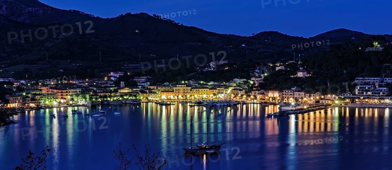 Panoramic view of Porto Azzurro with illuminated harbour promenade in the evening mood during blue hour