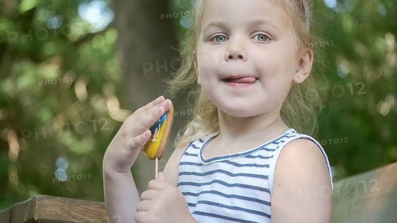 Little blonde girl holds gingerbread in Ukrainian national colors in her hand