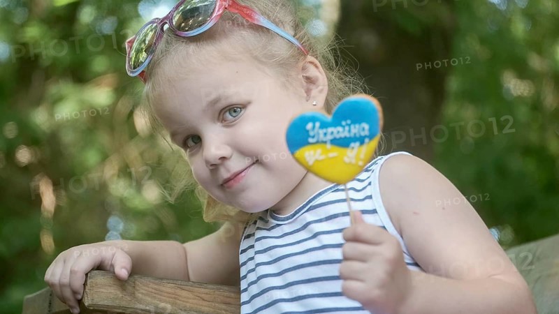 Little blonde girl holds gingerbread in Ukrainian national colors in her hand