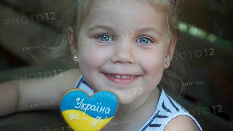 Little blonde girl holds gingerbread in Ukrainian national colors in her hand