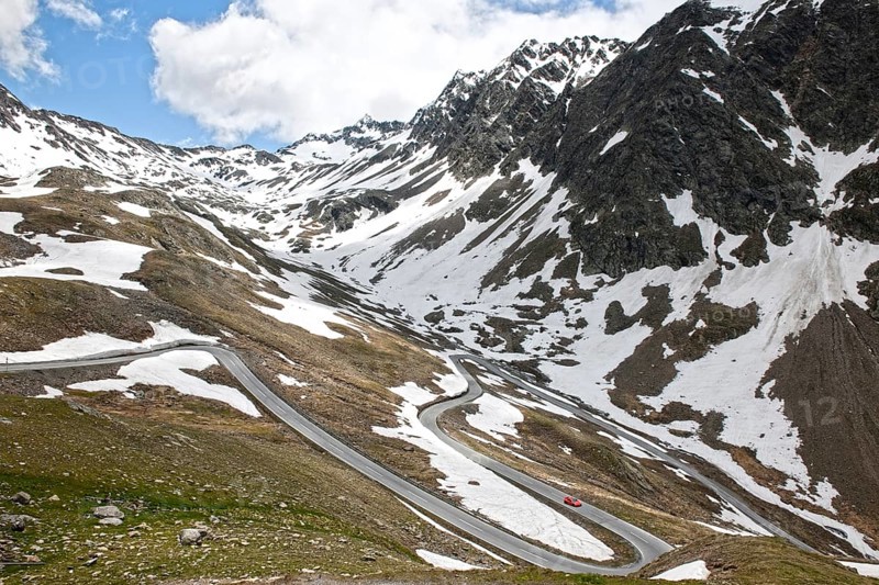 Red sports car Porsche drives into serpentine hairpin bend from Alpine pass on Timmelsjoch-Hochalpenstrasse