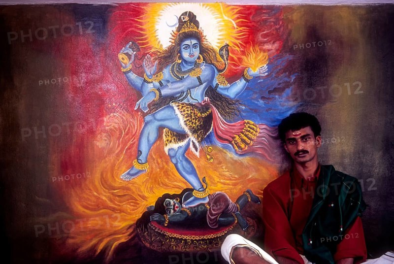 A man sitting near the mural of Lord shiva in Wadakancherry Siva Temple