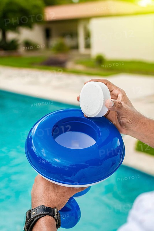 Hand of a pool disinfection worker holding a dispenser with a chlorine tablet. Hands holding a dispenser with pool chlorine tablet