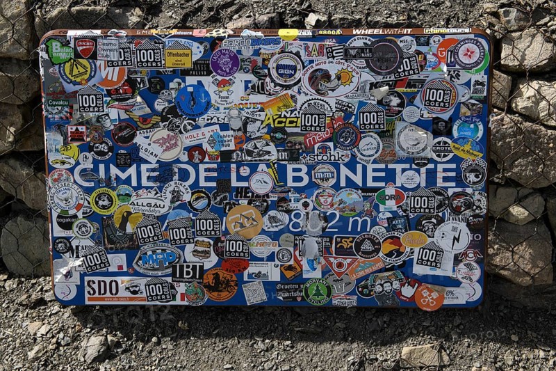 Sticker-covered official sign indicating altitude of 2802 metres above sea level from Cime de la Bonette