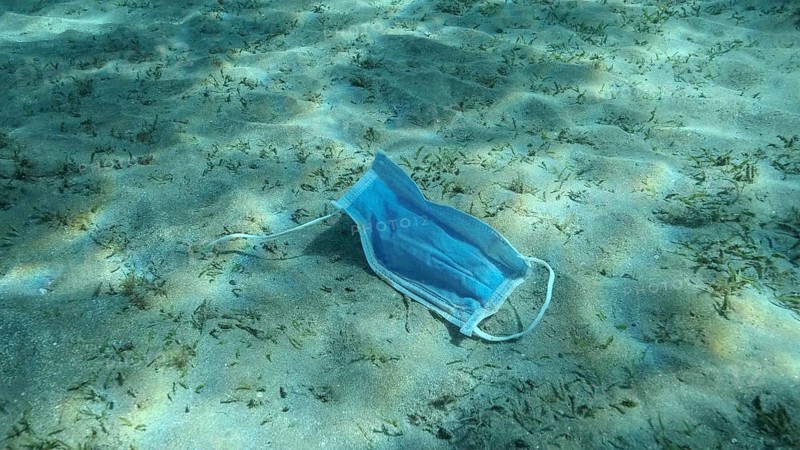 Used face mask lies on sandy bottom covered with green seagrass in sunlight. Discarded face masks polluting seabed since Coronavirus COVID-19. Pollution of Oceans. Red Sea