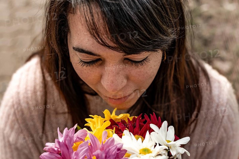 High angle view of a young woman smelling a bouquet of daisies in her hands. Close-up