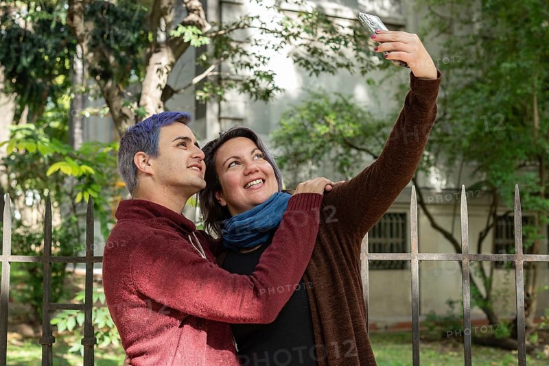 Two friends are taking selfies outdoors. He has blue hair