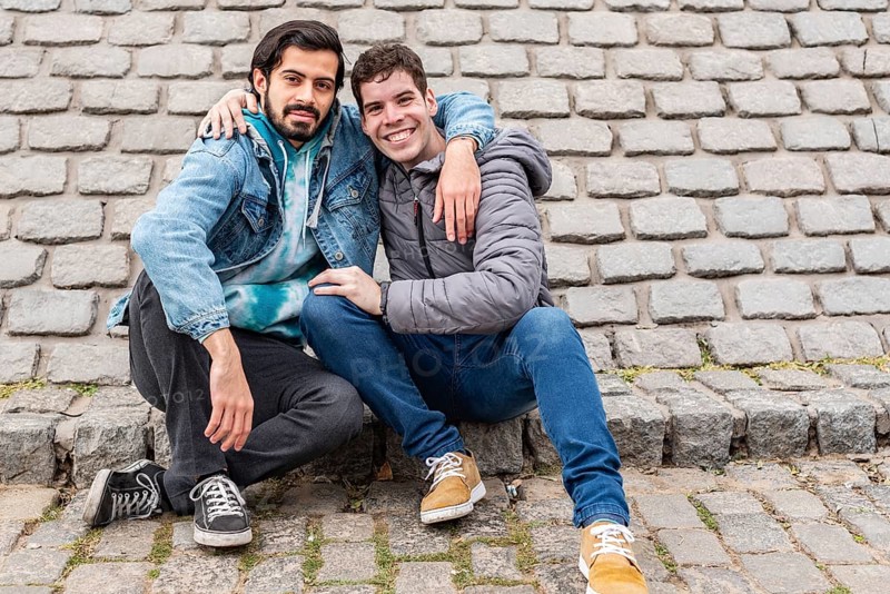 Two male friends hugging and looking at camera outdoors. Copy space