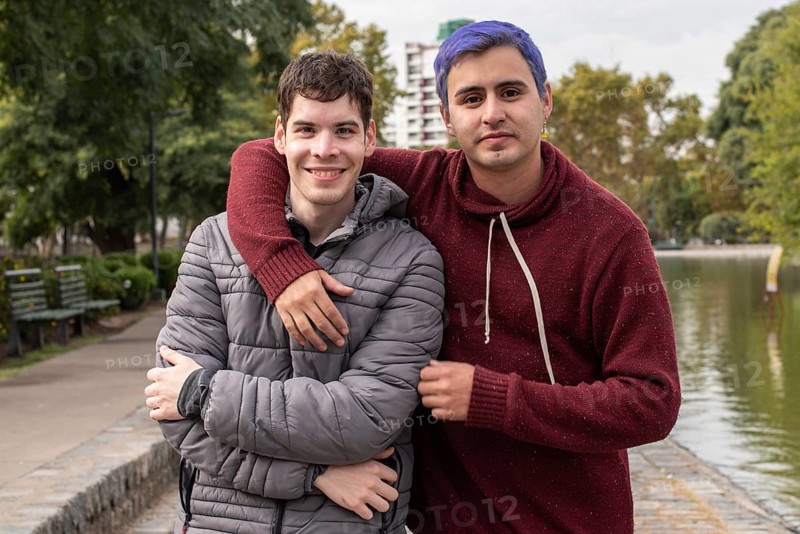 Gay male couple hugging and looking at camera outdoors