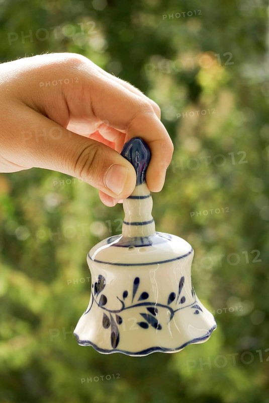 Hand holding a ceramic bell on a green background