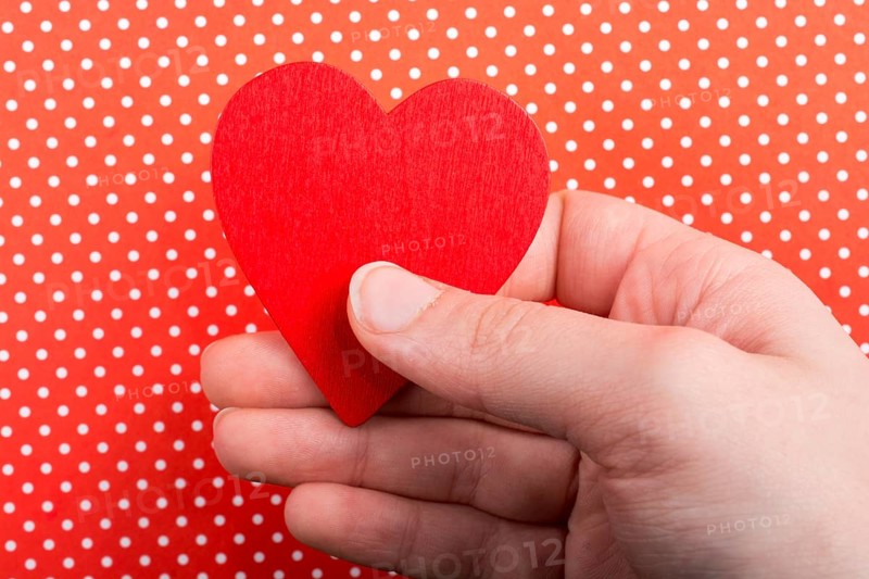 Red color heart shaped object in hand on dotted paper