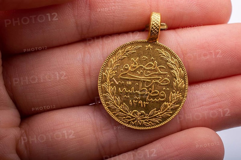 Turkish Ottoman style gold coin in hand on white background