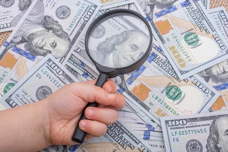 Magnifying glass is held over the banknote bundle of US dollar