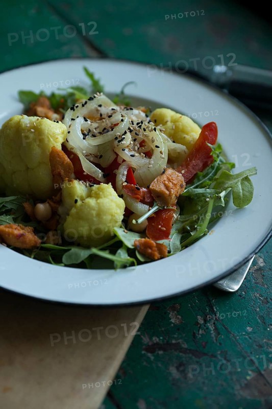 Vegan cauliflower salad on a tin plate with black cumin on a rustic table