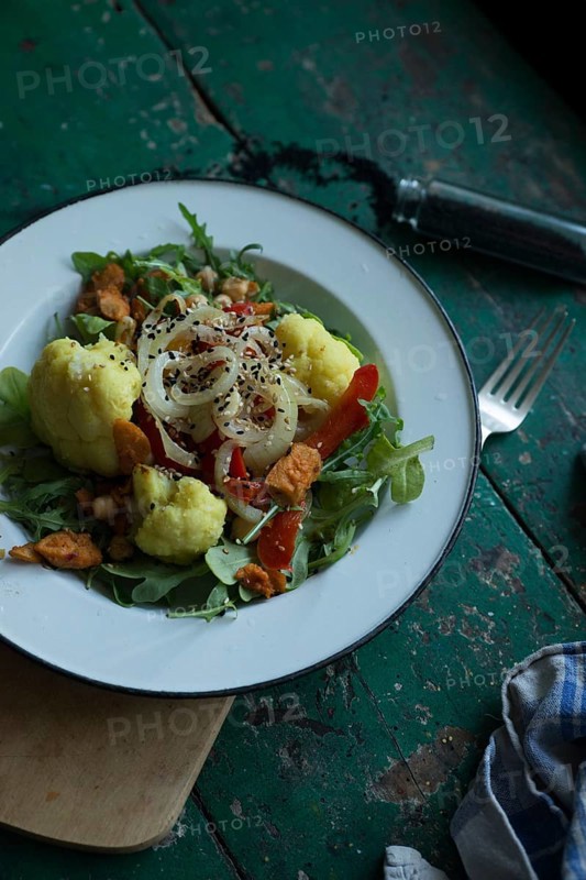 Vegan cauliflower salad on a tin plate with black cumin on a rustic table