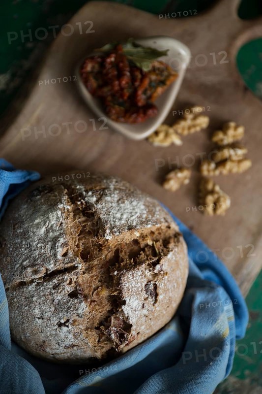 Freshly baked bread with walnuts and pickled tomatoes on a wooden board