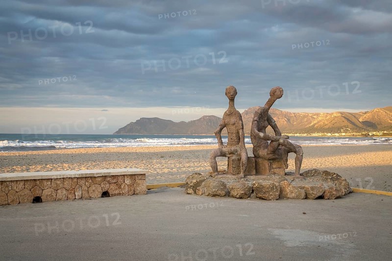 Sculptures by Joan Bennassar on beach promenade with sandy beach Playa Sa Canova in Son Serra de Marina, Serres de Llevant mountains in the back