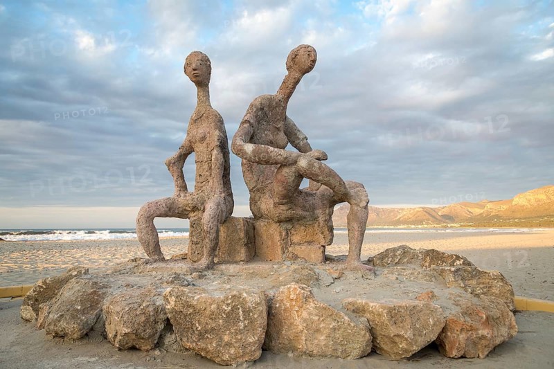 Sculptures by Joan Bennassar on beach promenade with sandy beach Playa Sa Canova in Son Serra de Marina, Serres de Llevant mountains in the back