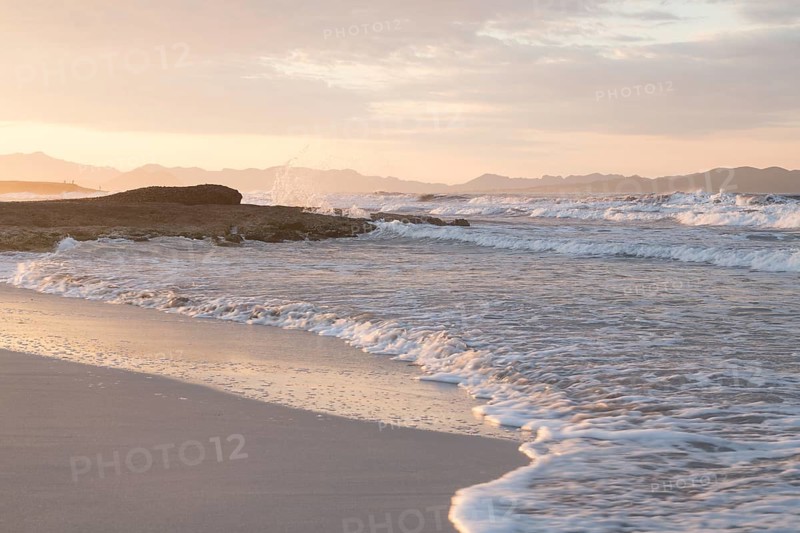 Sunset and breaking waves at the sandy beach playa in Son Serra de Marina, Tramuntana Mountains in the back
