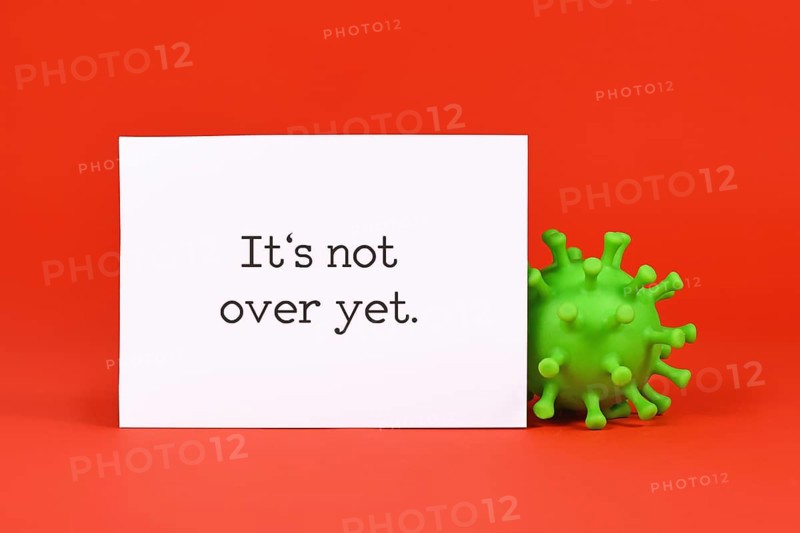 Corona virus model and note with text 'It's not over yet' on red background,