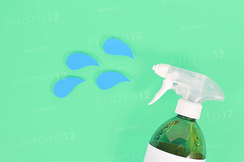 Green cleaning agent spray bottle with blue liquid drops cut from paper,