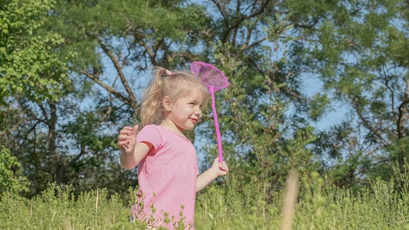Little girl plays with butterfly net of tall grass in city park. Cute little girl is playing with aerial insect net in meadow on sun day. Odessa, Ukraine