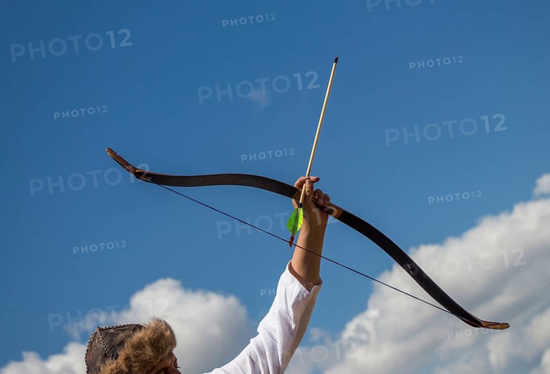 Archer with bow in traditional clothes shooting an arrow,