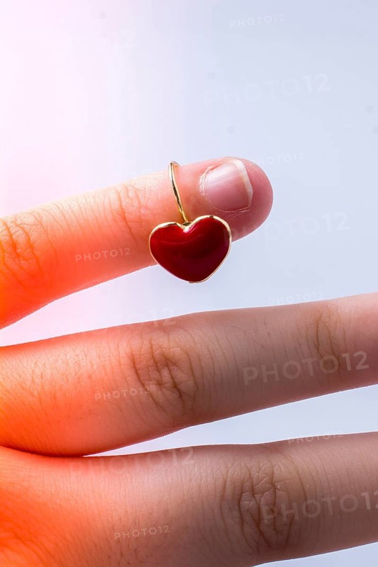 Red color heart shape earring in hand on white,