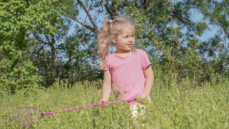 Little girl plays with butterfly net of tall grass in city park. Cute little girl is playing with aerial insect net in meadow on sun day. Odessa, Ukraine