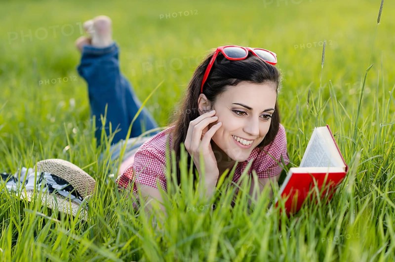 Young woman lying in meadow and reading a book,