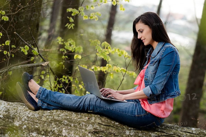 Young woman sitting in the forest with laptop,