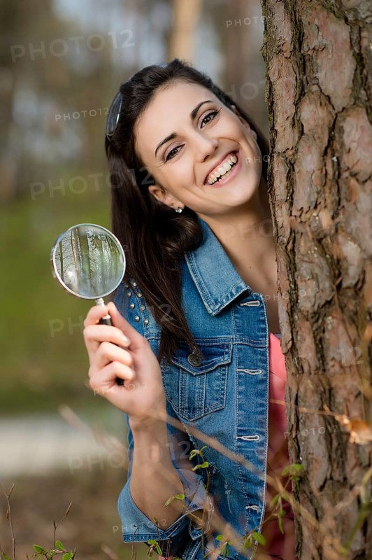 Woman looks at tree trunk under the magnifying glass,