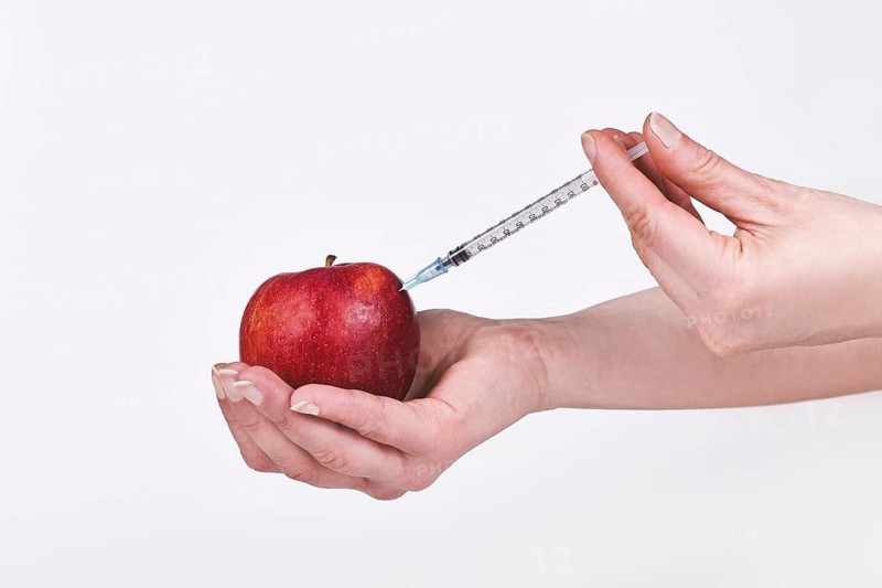 Apple being injected with syringe. Held by female hand,