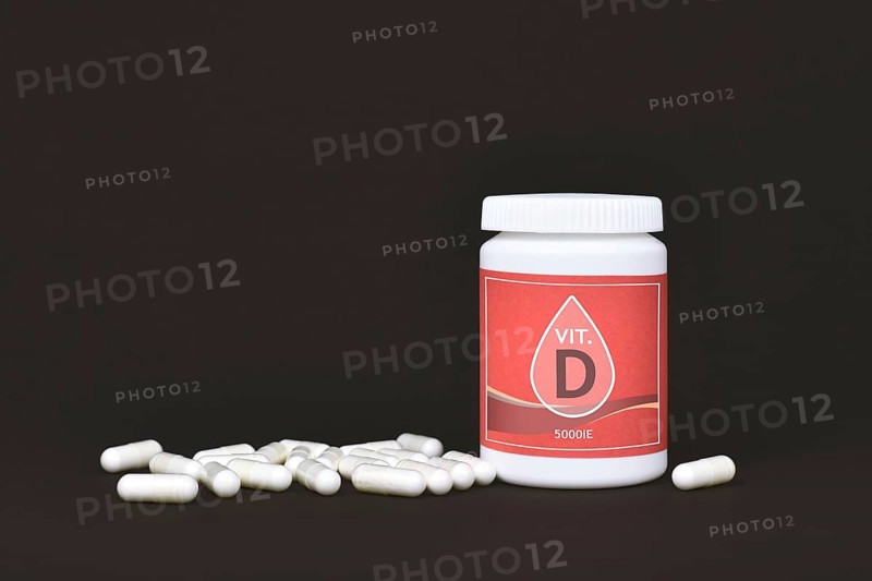 Vitamin D food supplement with container with pills on dark background,