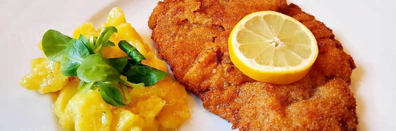 Delicious golden-brown fried Wiener Schnitzel with potato salad and a slice of lemon on a white plate,