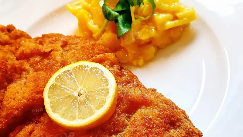 Delicious golden-brown fried Wiener Schnitzel with potato salad and a slice of lemon on a white plate,