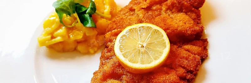 Delicious golden-brown fried Wiener Schnitzel with potato salad and a slice of lemon on a white plate,