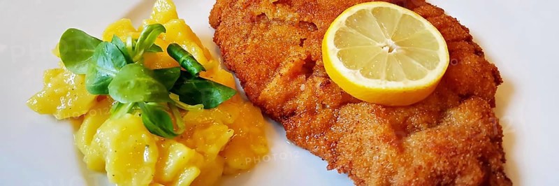Delicious golden-brown fried Wiener Schnitzel with potato salad and a slice of lemon on a white plate,
