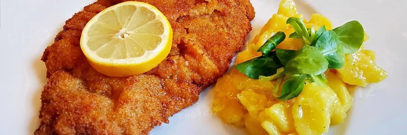 Delicious golden-brown fried Wiener Schnitzel with potato salad and a slice of lemon on a white plate,