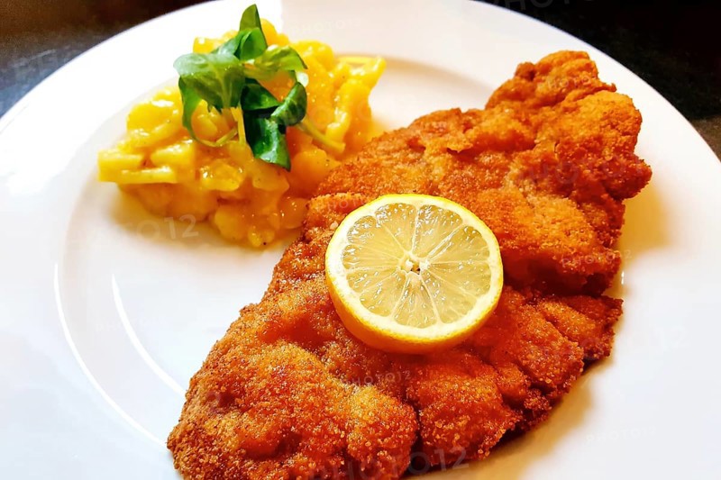 Delicious golden-brown fried Wiener Schnitzel with potato salad and a slice of lemon on a white plate,