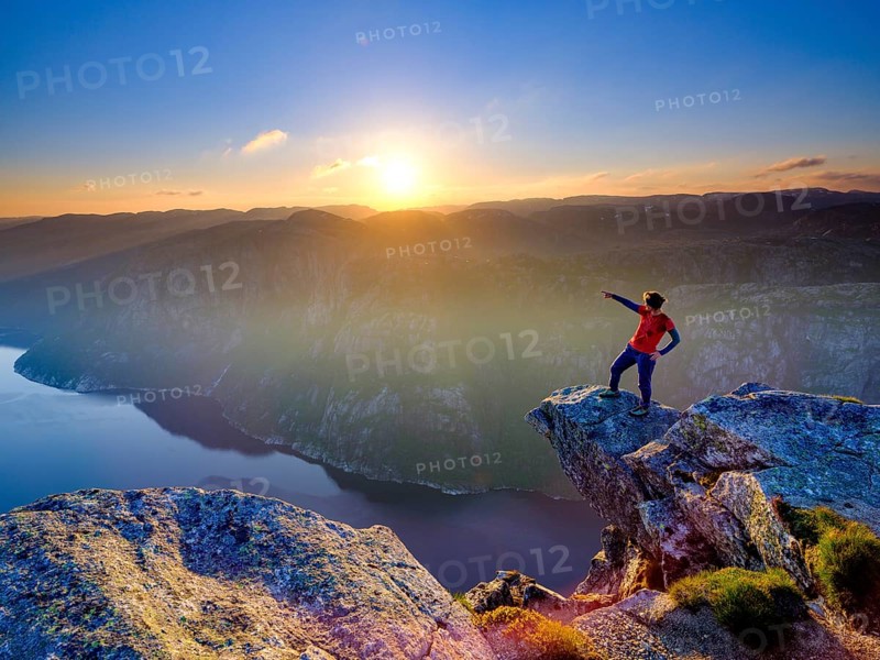 Woman standing on a rocky outcrop at Kjerag above the Lysefjord pointing her finger into the distance, sunset