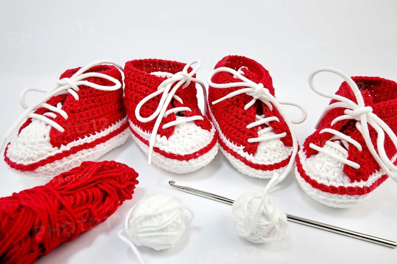 Baby shoes or crochet shoes in red and white isolated against a white background,