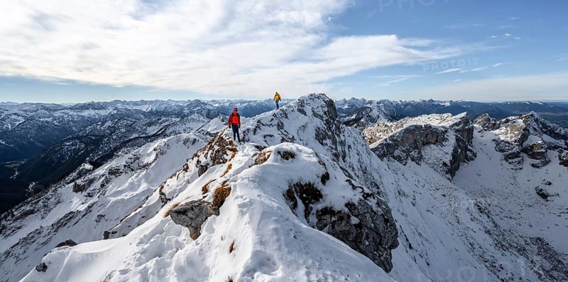 Two mountaineers on a narrow rocky snowy ridge, behind peak crow