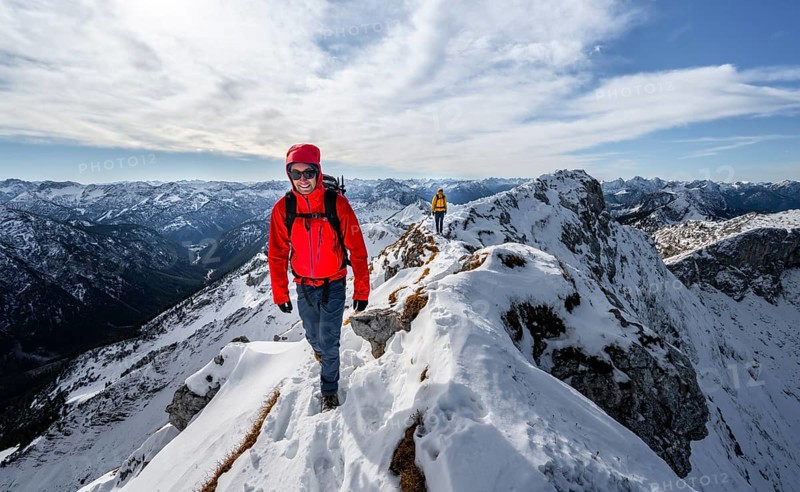 Two mountaineers on a narrow rocky snowy ridge, behind peak crow