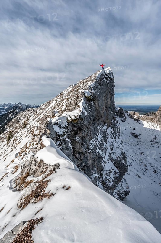 Mountaineer stretching his arms in the air, standing on a snow-covered rocky ridge