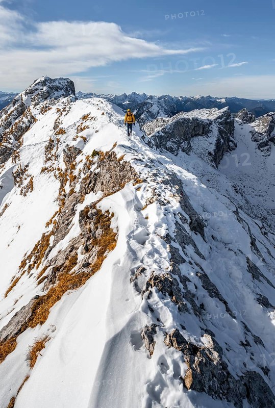 Climbers on a narrow rocky snowy ridge, behind peak crow