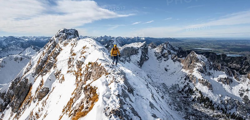 Climbers on a narrow rocky snowy ridge, behind peak crow