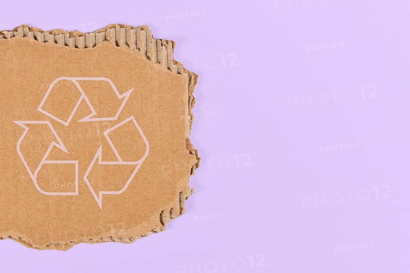 Piece of cardboard with recycling arrow sign on violet blue background with copy space,