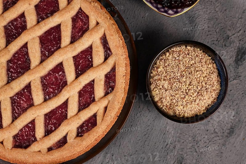 Close up of pie called Linzer Torte, a traditional Austrian shortcake pastry topped with fruit preserves and sliced nuts with lattice design next to bowl with ground almonds
